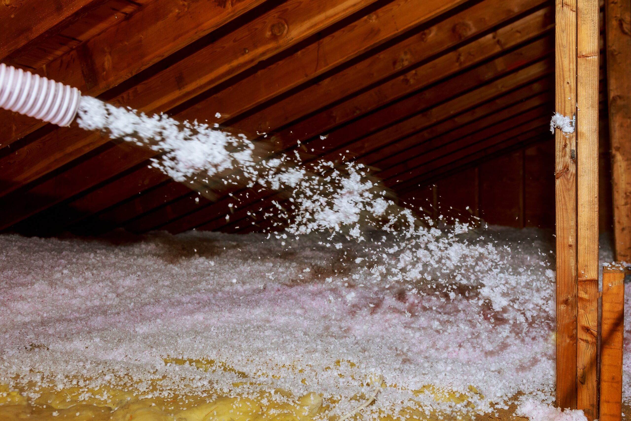 worker spraying mineral rock wool of house attic insulation