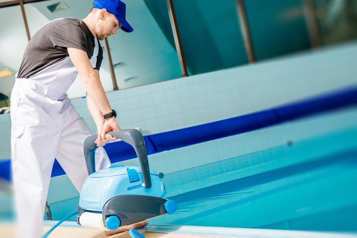 swimming pool technician with automated pool cleaner preparing for cleaning.
