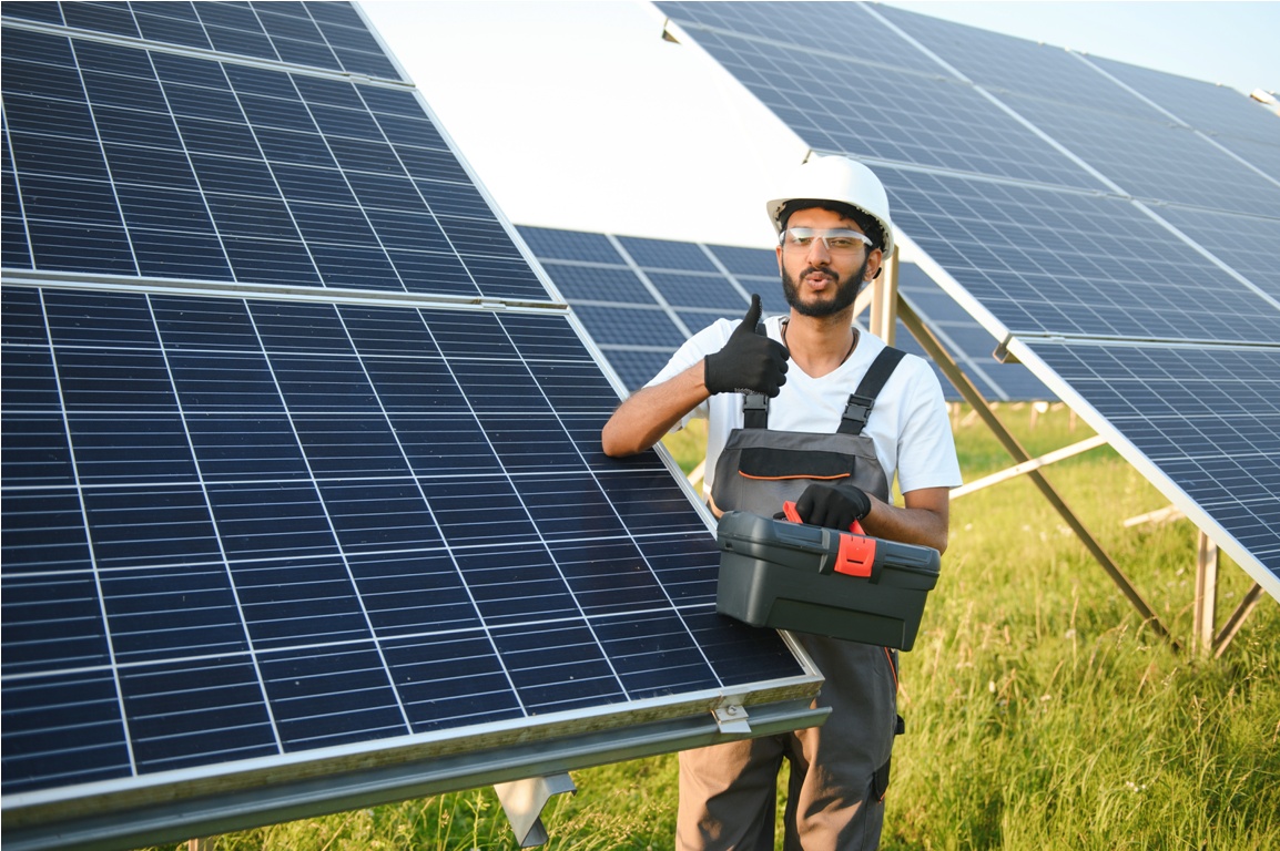 an indian worker in uniform and with tools works on a solar panel farm.