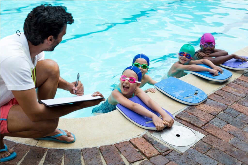 instructor writing on clipboard with swimmers at poolside