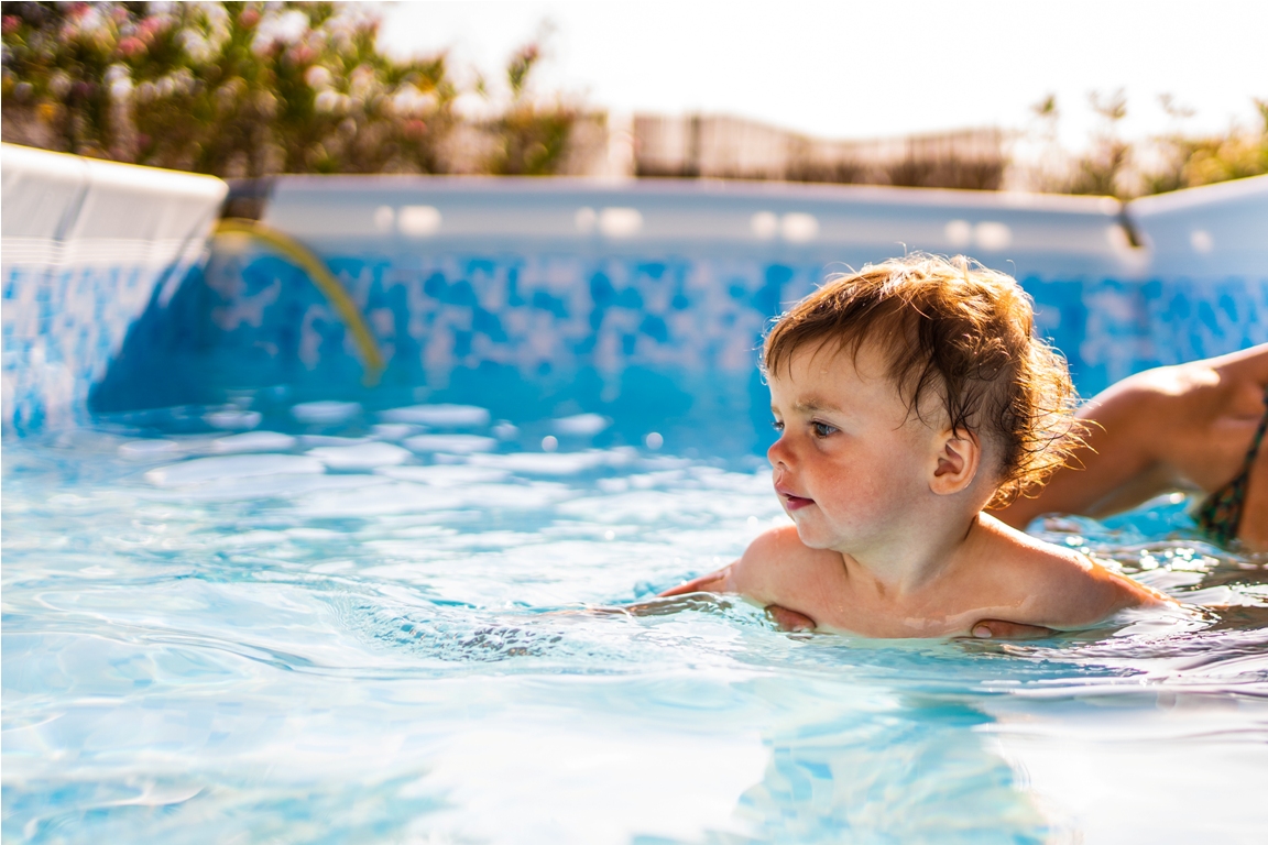 little girl swimming in a household swimming pool next to her mother