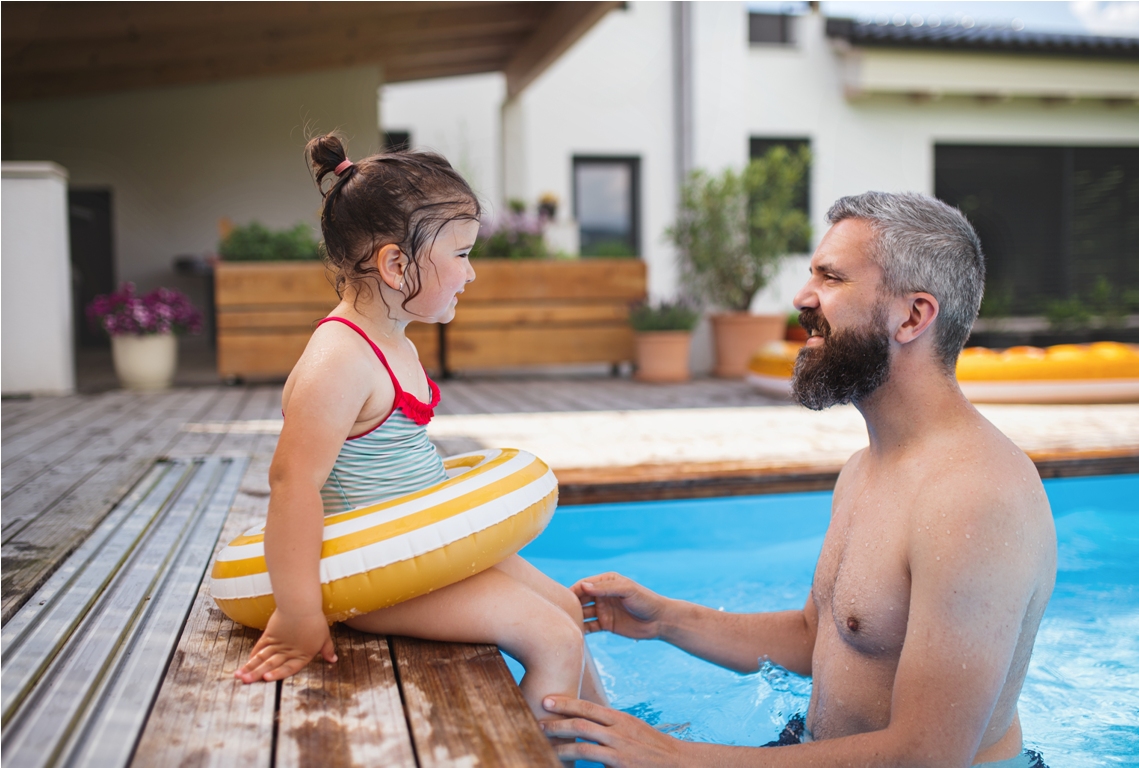 father with happy daughter outdoors in the backyard, playing in swimming pool.