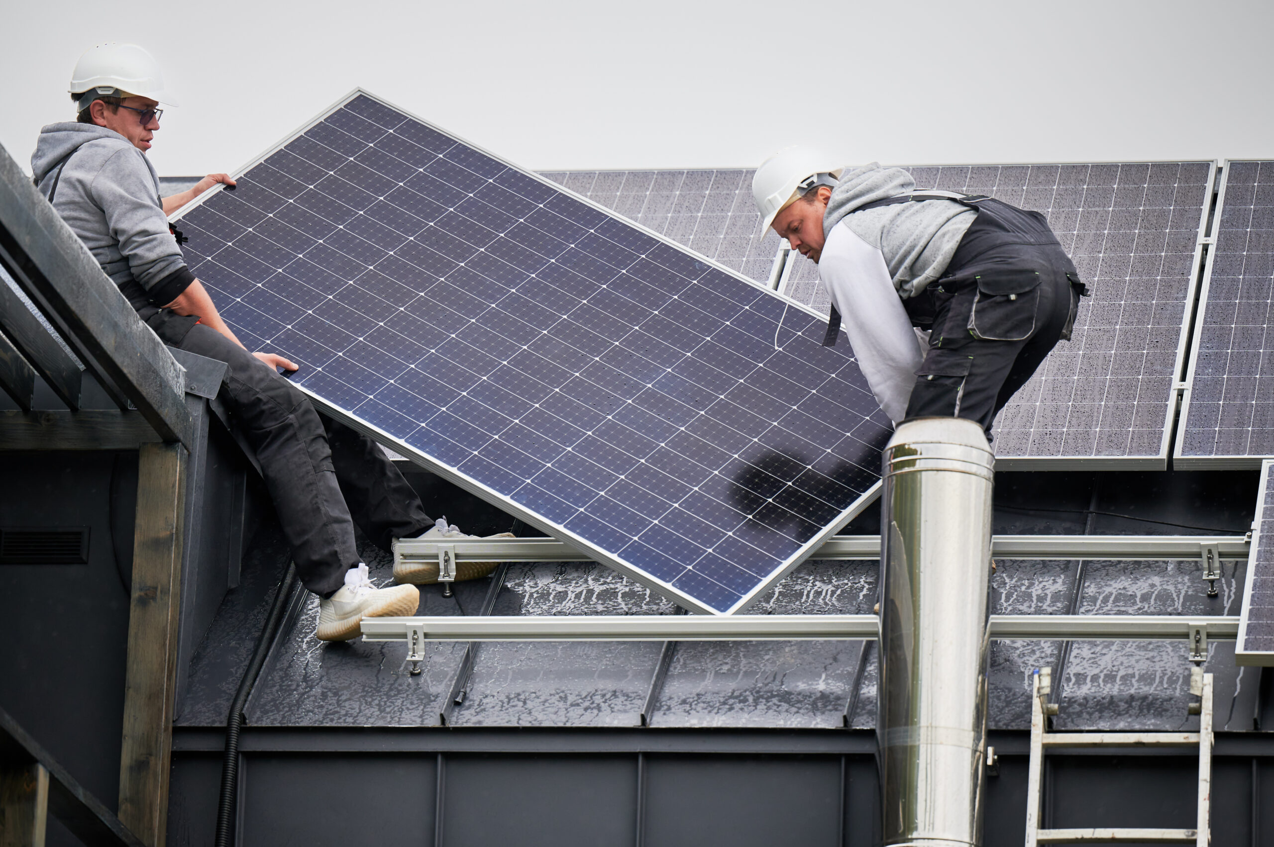 technicians carrying photovoltaic solar module while installing solar panel system on roof of house