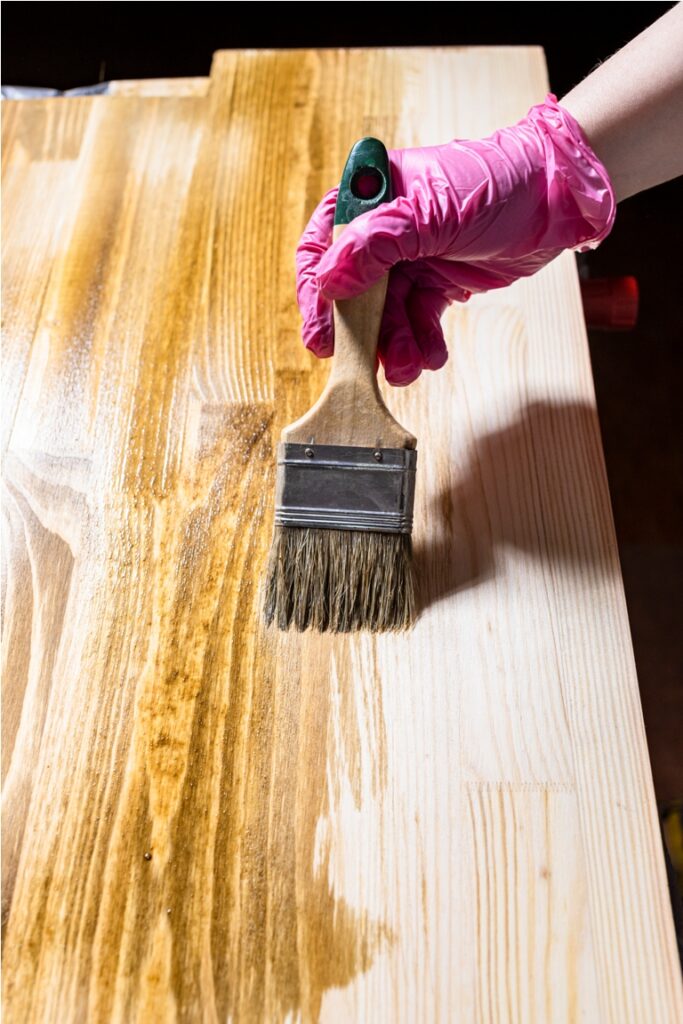 solid board is hued with wood stain by paintbrush