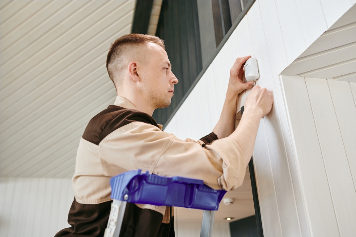young man in uniform putting alarm system on wall of house